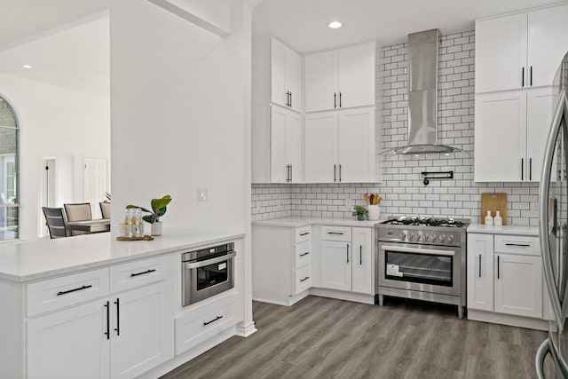 kitchen featuring dark wood-type flooring, white cabinets, wall chimney exhaust hood, and stainless steel appliances