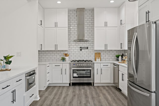 kitchen featuring appliances with stainless steel finishes, wall chimney exhaust hood, white cabinetry, and light hardwood / wood-style flooring