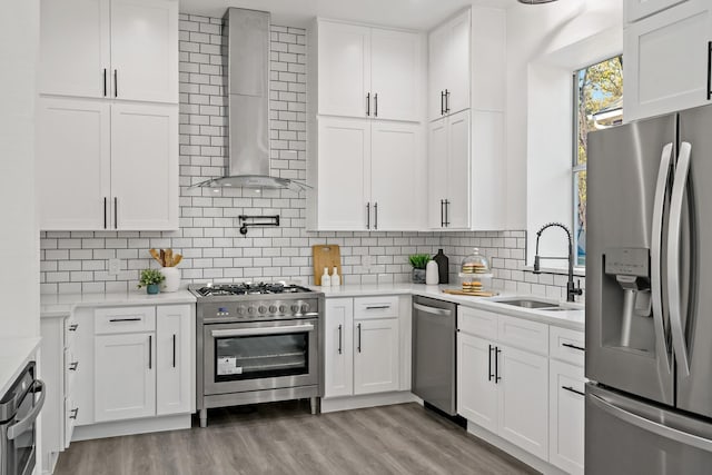 kitchen featuring wall chimney exhaust hood, white cabinetry, stainless steel appliances, light hardwood / wood-style floors, and sink