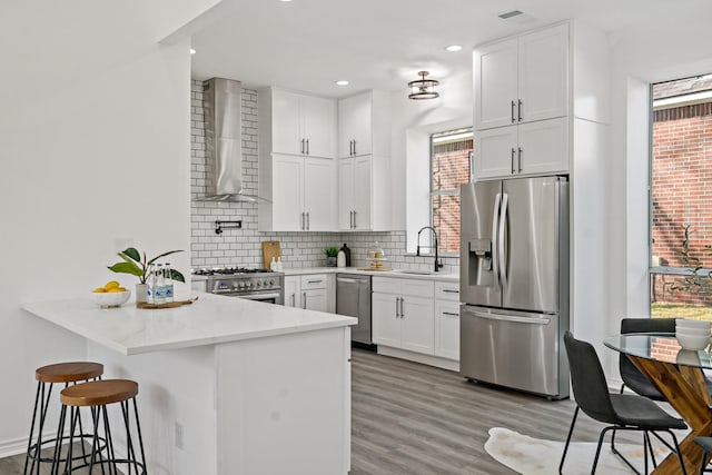 kitchen featuring tasteful backsplash, white cabinetry, light stone countertops, appliances with stainless steel finishes, and wall chimney exhaust hood