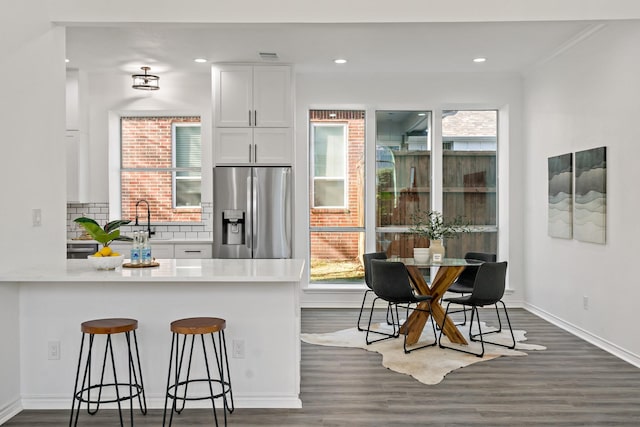 kitchen featuring a kitchen bar, white cabinetry, dark hardwood / wood-style flooring, stainless steel fridge, and kitchen peninsula