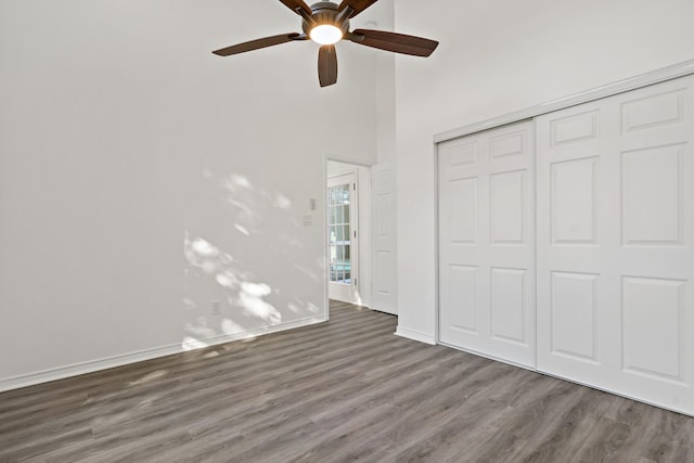 unfurnished bedroom with ceiling fan, a high ceiling, dark hardwood / wood-style floors, and a closet