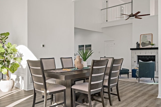 dining area with a high ceiling, ceiling fan, a tiled fireplace, and hardwood / wood-style floors