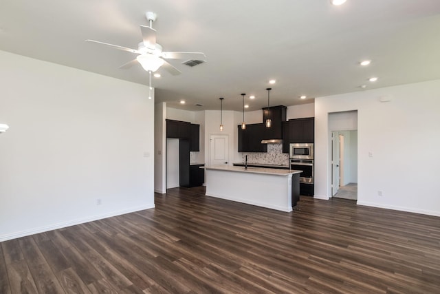 kitchen featuring dark hardwood / wood-style floors, appliances with stainless steel finishes, backsplash, and an island with sink