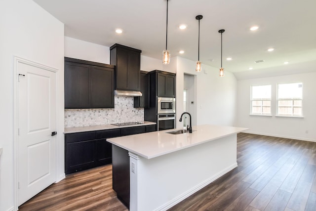 kitchen with tasteful backsplash, pendant lighting, sink, an island with sink, and dark hardwood / wood-style flooring