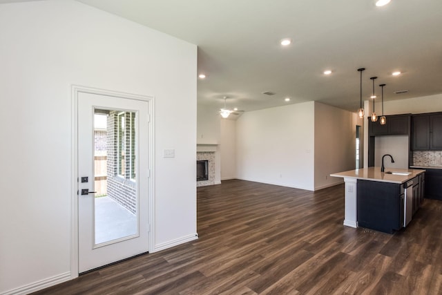 kitchen with decorative light fixtures, dark hardwood / wood-style flooring, sink, backsplash, and a kitchen island with sink