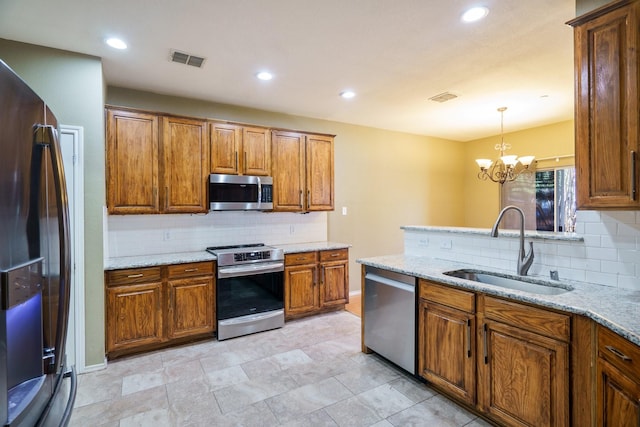 kitchen with light stone countertops, stainless steel appliances, sink, hanging light fixtures, and a chandelier