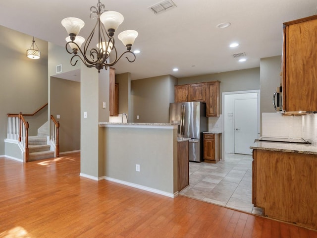 kitchen with backsplash, light hardwood / wood-style floors, an inviting chandelier, hanging light fixtures, and appliances with stainless steel finishes