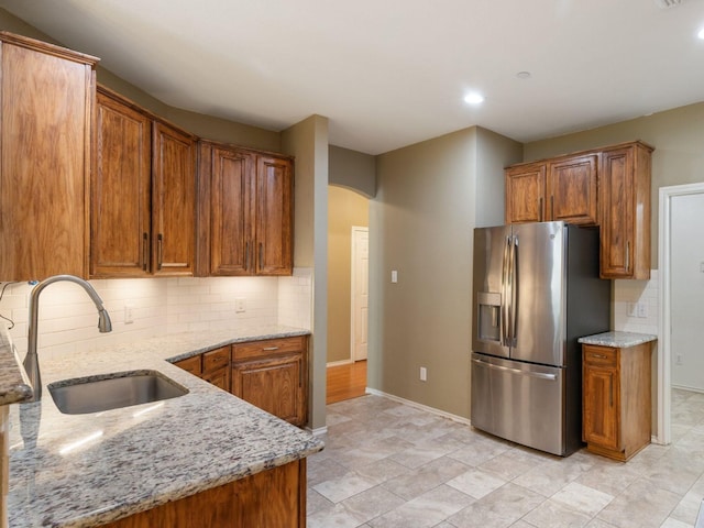 kitchen featuring backsplash, stainless steel fridge, sink, and light stone counters