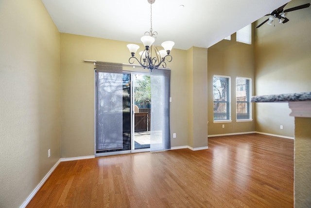 empty room with ceiling fan with notable chandelier, a wealth of natural light, and hardwood / wood-style flooring