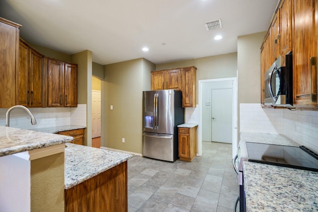 kitchen with light stone countertops, backsplash, appliances with stainless steel finishes, and sink