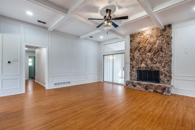 unfurnished living room with light hardwood / wood-style floors, coffered ceiling, a stone fireplace, and beamed ceiling