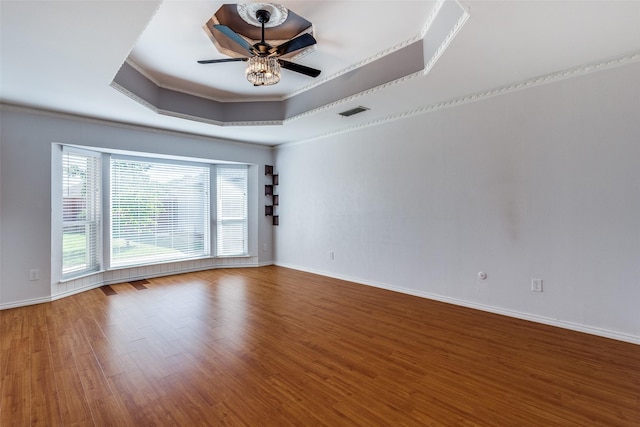 empty room with ceiling fan, a raised ceiling, crown molding, and hardwood / wood-style floors