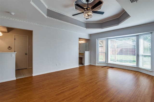 spare room with ceiling fan, light wood-type flooring, crown molding, and a raised ceiling