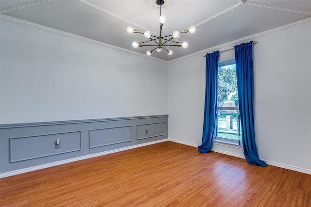 unfurnished room featuring a healthy amount of sunlight, wood-type flooring, an inviting chandelier, and ornamental molding