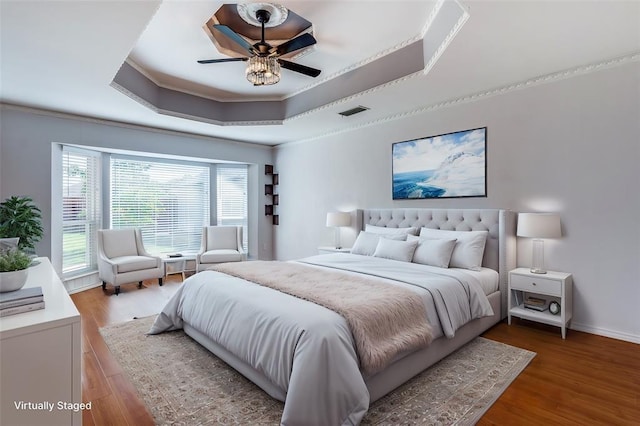 bedroom featuring ceiling fan, wood finished floors, baseboards, a raised ceiling, and crown molding