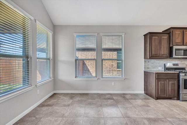 kitchen featuring lofted ceiling, stainless steel appliances, tasteful backsplash, light tile patterned floors, and dark brown cabinets