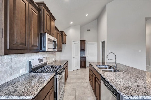 kitchen featuring a kitchen island with sink, sink, light stone counters, and stainless steel appliances