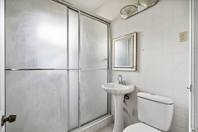 bathroom with toilet, tile walls, and a shower with door