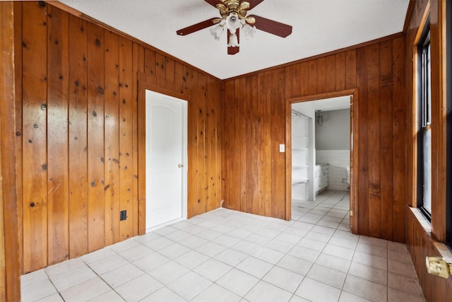 unfurnished room with ceiling fan, crown molding, light tile patterned flooring, and wood walls