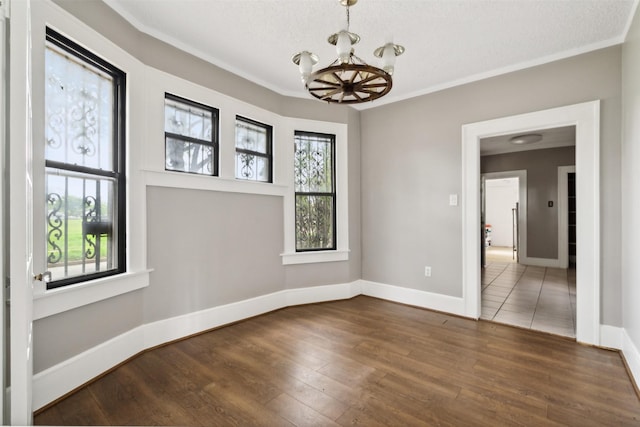 unfurnished room featuring dark wood-type flooring, an inviting chandelier, crown molding, and plenty of natural light