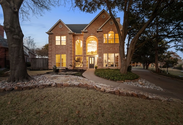 traditional-style house featuring brick siding, fence, a chimney, and a front lawn