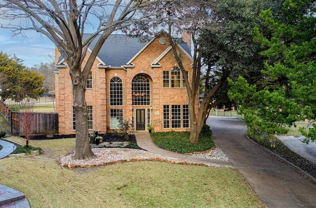 traditional home with brick siding, a chimney, roof with shingles, fence, and a front yard