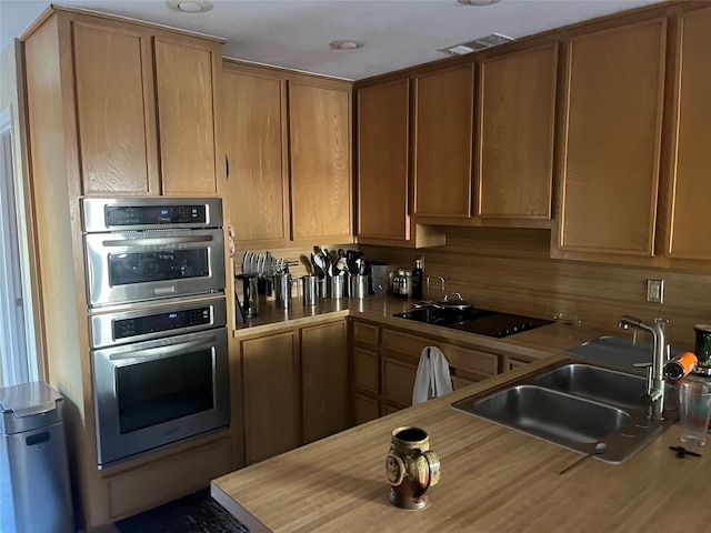 kitchen with tasteful backsplash, wooden counters, sink, double oven, and black electric cooktop