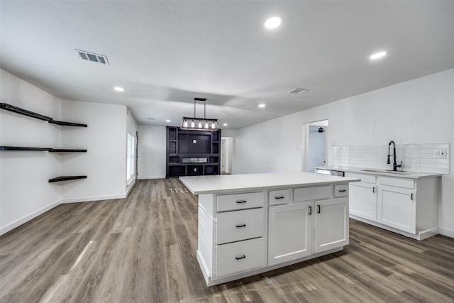 kitchen with pendant lighting, white cabinets, a kitchen island, sink, and light wood-type flooring