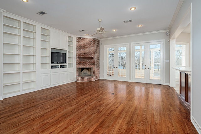 unfurnished living room featuring hardwood / wood-style flooring, ceiling fan, crown molding, a brick fireplace, and french doors