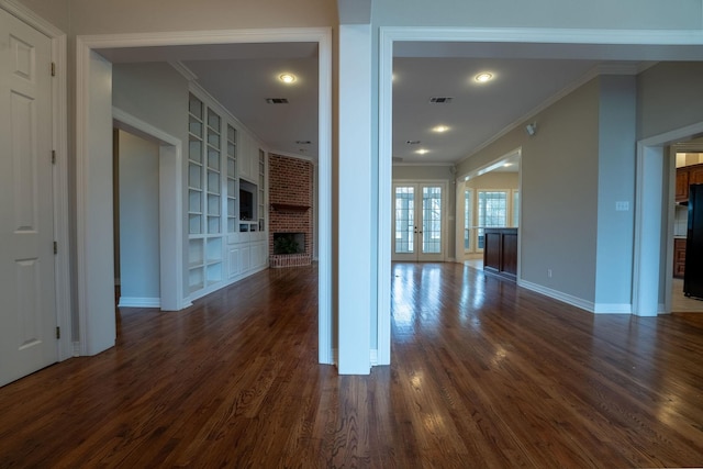 unfurnished living room featuring a fireplace, french doors, ornamental molding, dark wood-type flooring, and built in shelves