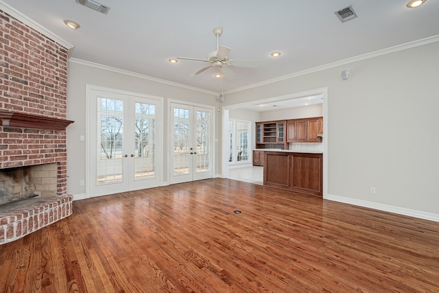 unfurnished living room featuring a fireplace, ceiling fan, light hardwood / wood-style floors, crown molding, and french doors