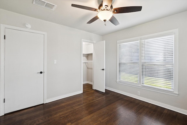 unfurnished bedroom featuring ceiling fan, dark wood-type flooring, a closet, and a walk in closet