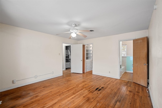 unfurnished bedroom featuring ensuite bathroom, ceiling fan, a closet, a walk in closet, and light hardwood / wood-style flooring