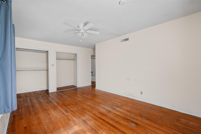 unfurnished bedroom with ceiling fan, two closets, and wood-type flooring