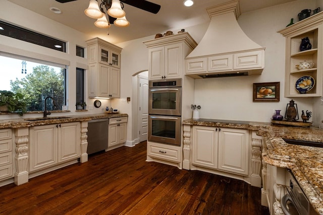 kitchen with ceiling fan, appliances with stainless steel finishes, custom range hood, light stone countertops, and sink