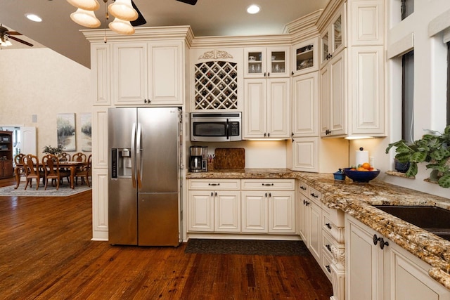 kitchen with ceiling fan, dark wood-type flooring, appliances with stainless steel finishes, cream cabinetry, and light stone counters