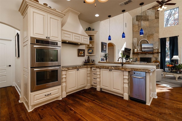 kitchen with kitchen peninsula, ceiling fan, decorative light fixtures, custom range hood, and double oven