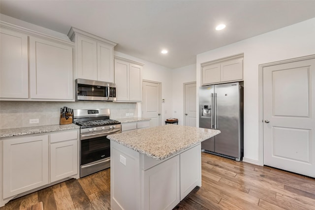 kitchen with backsplash, light hardwood / wood-style floors, a center island, light stone countertops, and appliances with stainless steel finishes