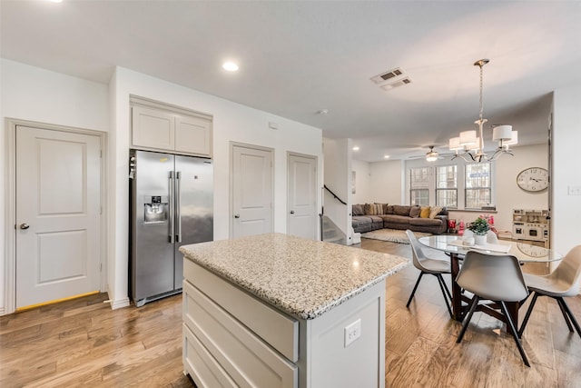 kitchen with a kitchen island, pendant lighting, stainless steel refrigerator with ice dispenser, light hardwood / wood-style flooring, and ceiling fan with notable chandelier