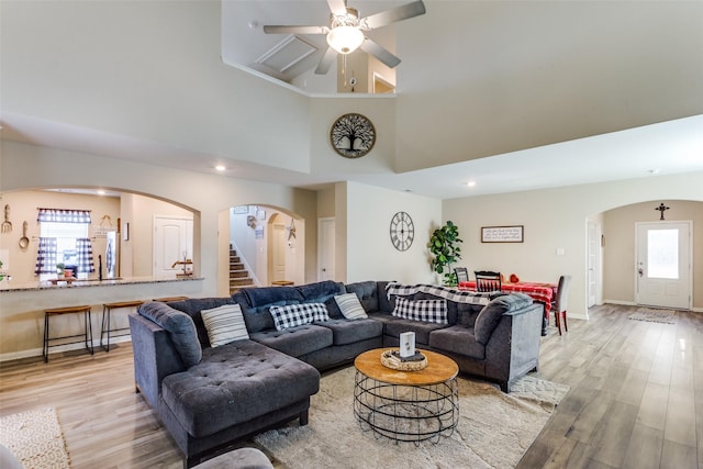 living room with ceiling fan, a high ceiling, and light hardwood / wood-style floors