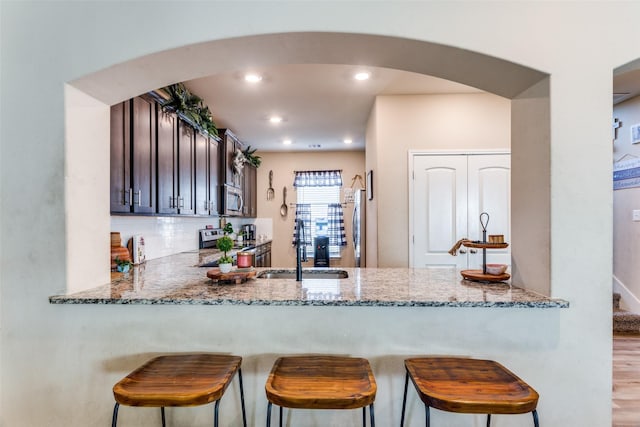 kitchen featuring kitchen peninsula, appliances with stainless steel finishes, light stone counters, dark brown cabinetry, and sink