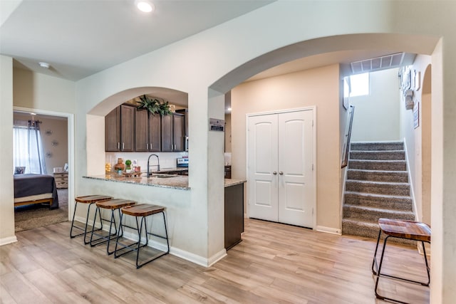 kitchen featuring light stone countertops, dark brown cabinetry, sink, kitchen peninsula, and light wood-type flooring