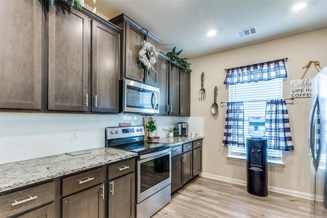 kitchen with appliances with stainless steel finishes, tasteful backsplash, light wood-type flooring, dark brown cabinets, and light stone counters