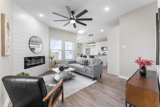 living room with a fireplace, recessed lighting, light wood-style floors, ceiling fan, and baseboards