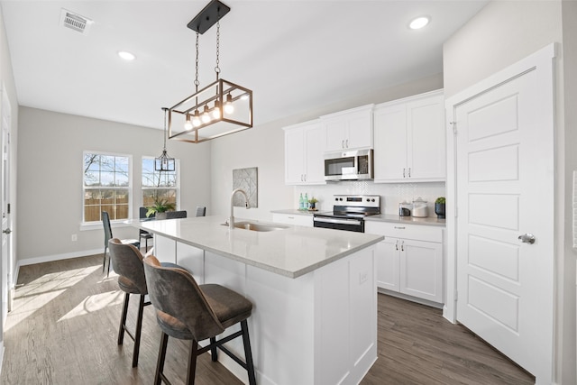 kitchen with appliances with stainless steel finishes, a center island with sink, a sink, and white cabinetry