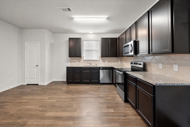 kitchen with hardwood / wood-style floors, appliances with stainless steel finishes, dark brown cabinetry, backsplash, and light stone counters