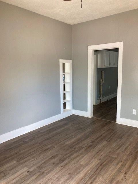 empty room featuring ceiling fan, dark wood-type flooring, a textured ceiling, and built in features