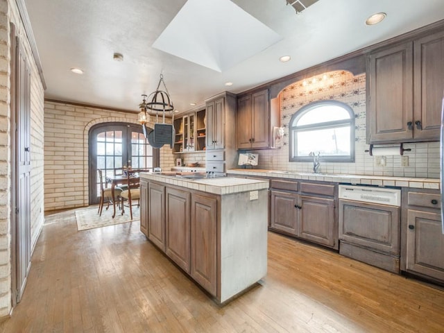 kitchen with tile counters, brick wall, dishwasher, a kitchen island, and sink