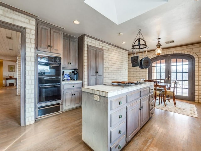 kitchen featuring stainless steel gas stovetop, tile counters, black double oven, french doors, and a kitchen island